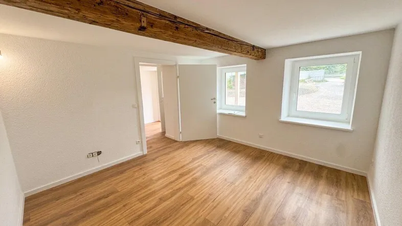 Helles Zimmer mit Holzbalken an der Decke und Laminatboden, bereit zur individuellen Gestaltung.