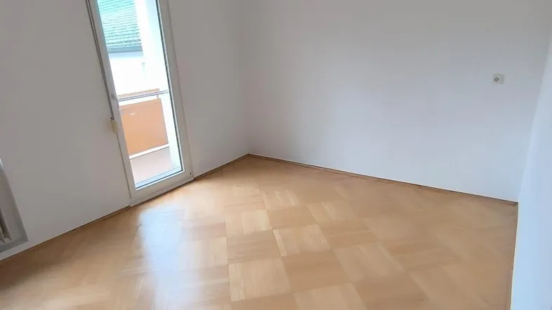 Heller Raum mit Parkettboden und Zugang zu einem Außenbereich, ideal als Wohn- oder Schlafzimmer.