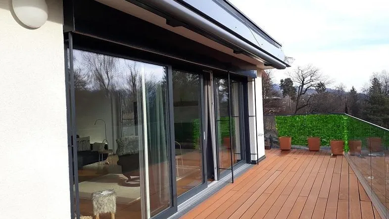 Geräumige Terrasse mit Holzbelag, Glasgeländer und Blick ins Grüne, direkt vom Wohnbereich zugänglich.