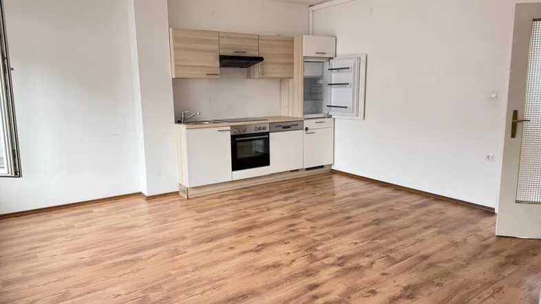 Kleine Einbauküche mit hellen Holzfronten und Laminatboden in einem offenen Raum.