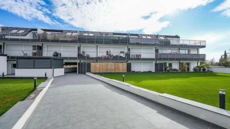 Moderne Wohnanlage mit gepflegter Rasenfläche und Zugangsweg unter blauem Himmel.