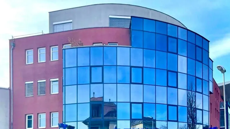 Moderne Bürogebäude-Fassade mit auffälliger blauer Glasfront und roten Akzenten unter klarem Himmel.