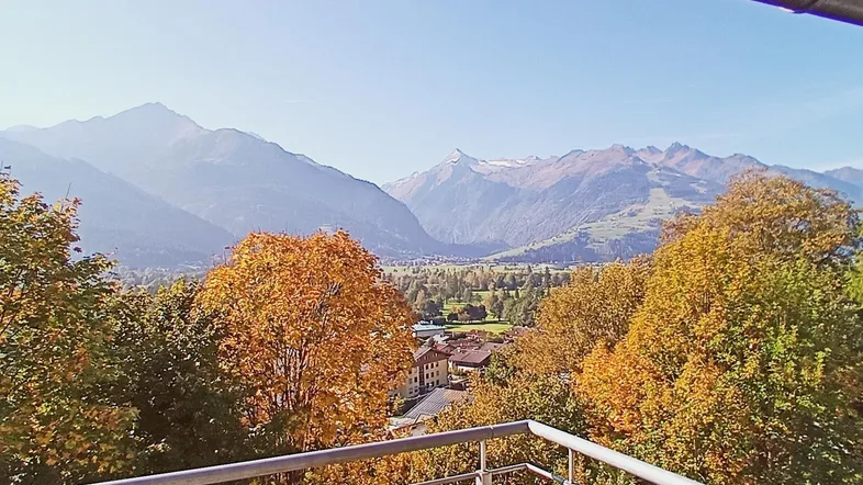 Sonniger Balkon mit weitem Blick auf die majestätische Berglandschaft und herbstliche Bäume.