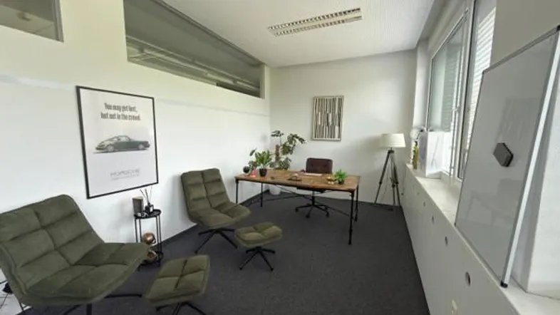 Geräumiges Büro mit modernem Schreibtisch, bequemen Sesseln und großen Fenstern für viel Tageslicht.