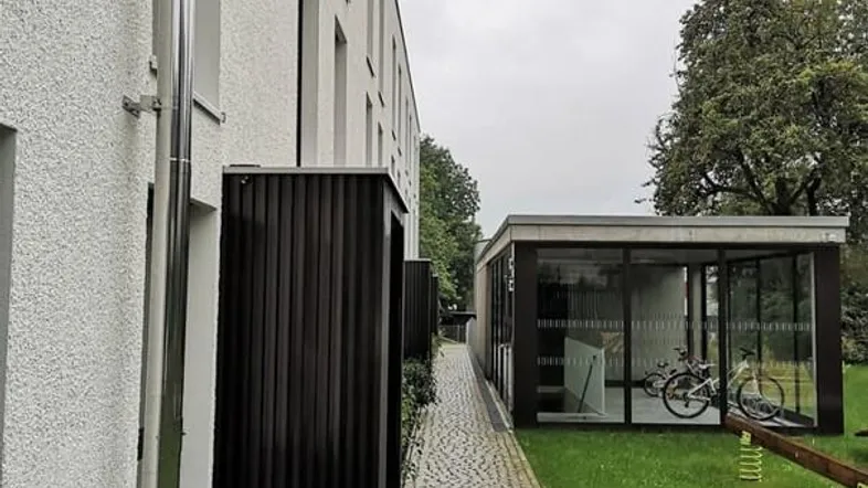 Gebäudeansicht mit gepflastertem Weg, Grünflächen und einem modernen Fahrradraum.