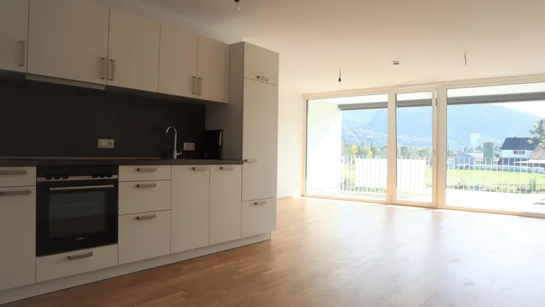 Moderne Küche mit weißen Schränken und Holzboden, offen zum Wohnbereich mit Bergblick.