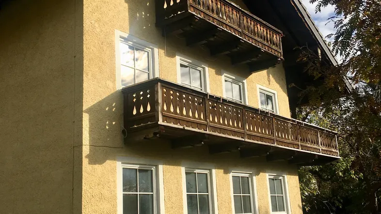 Traditionelles Haus mit gelber Fassade und zwei Holzbalkonen unter einem Satteldach.