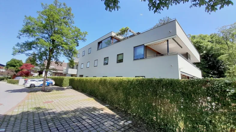Modernes Mehrfamilienhaus mit Flachdach und gepflegter Hecke in grüner Umgebung.