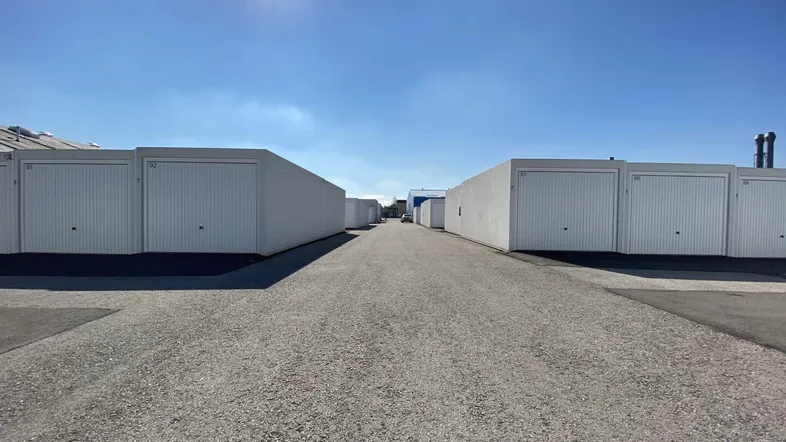 Reihe von weißen Garagenboxen unter strahlend blauem Himmel mit Schotterweg im Vordergrund.