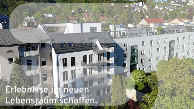 Moderne Wohnanlage mit mehreren Gebäuden, Balkonen und grüner Umgebung, eingebettet in eine hügelige Landschaft.
