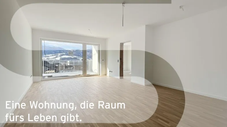 Heller, leerer Wohnraum mit Holzboden, großen Fenstern und Zugang zum Balkon mit Bergblick.