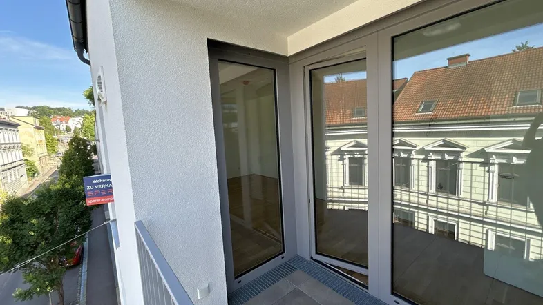 Heller Balkon mit Fliesenboden und Blick auf die Straße sowie gegenüberliegende Gebäude.