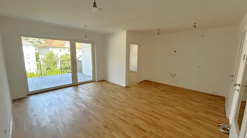 Helles, leeres Wohnzimmer mit Holzboden und Zugang zu einem Balkon, bereit für die Einrichtung.
