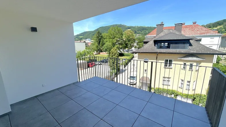 Geräumiger Balkon mit modernen grauen Fliesen und weitem Blick ins Grüne und auf umliegende Gebäude.