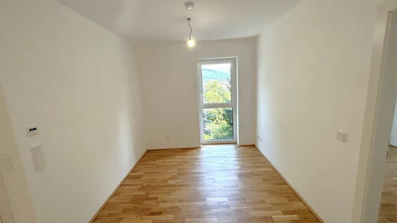 Helles Zimmer mit Holzboden und Blick ins Grüne, ideal als Schlaf- oder Wohnbereich.