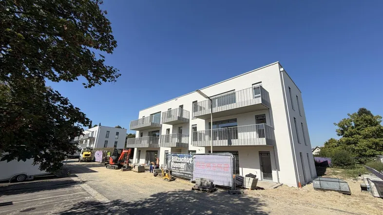 Modernes Neubau-Mehrfamilienhaus mit weißen Fassaden und Balkonen, umgeben von Baustellenaktivitäten.