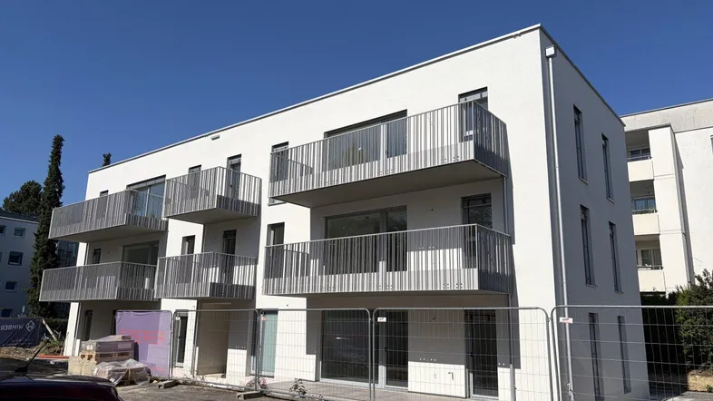 Modernes Mehrfamilienhaus im Bau mit weißen Fassaden und mehreren Balkonen unter blauem Himmel.