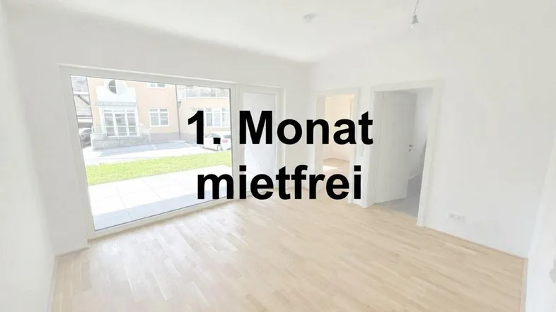 Heller, unmöblierter Raum mit Holzboden und großen Fenstern, die Zugang zu einer Terrasse und einem Garten bieten.