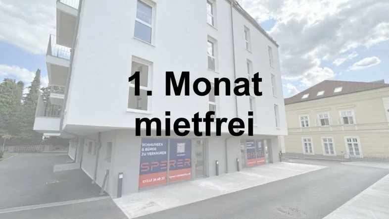 Modernes weißes Mehrfamilienhaus mit Balkonen und Geschäftsflächen im Erdgeschoss, beworben mit einem mietfreien Monat.