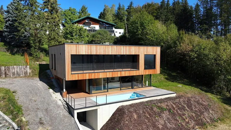 Modernes Haus mit Holzfassade, großen Fenstern und integriertem Pool in Hanglage.