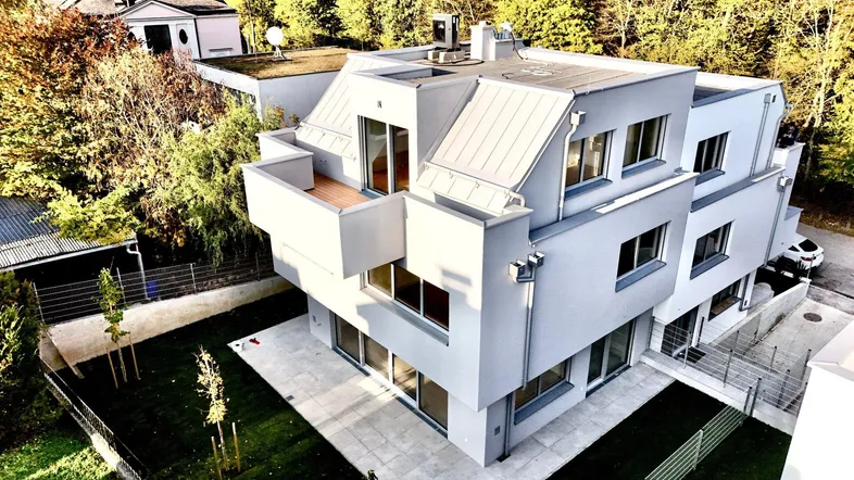 Moderne Architektur eines Mehrfamilienhauses mit Flachdach und Balkonen, umgeben von Bäumen.