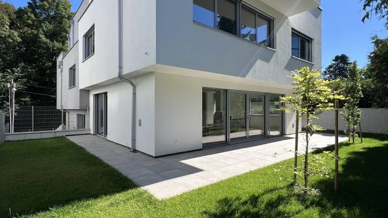 Moderne weiße Villa mit Flachdach, großer Terrasse und gepflegtem Rasen unter blauem Himmel.