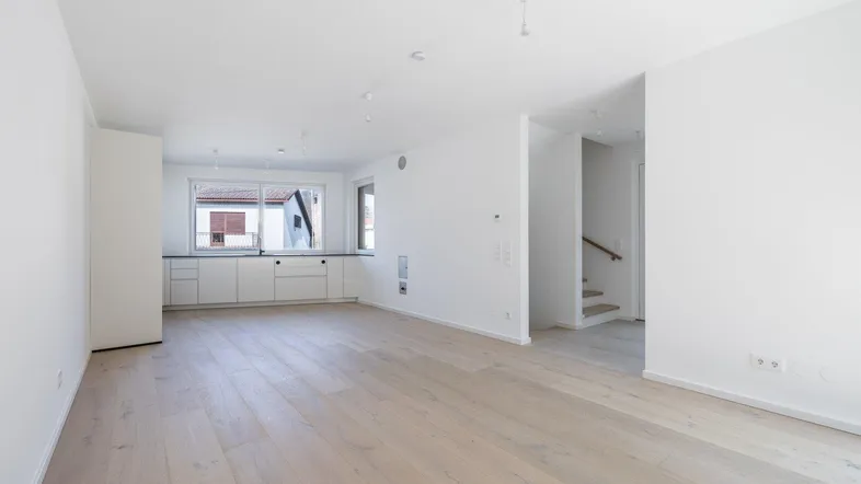 Heller, offener Wohnbereich mit Holzboden und integrierter Küchenzeile, ideal für modernes Wohnen.
