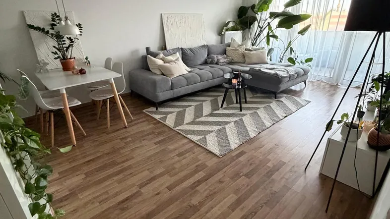 Helles Wohn- und Esszimmer mit modernem Sofa, Holzboden und Zugang zu einem Balkon.