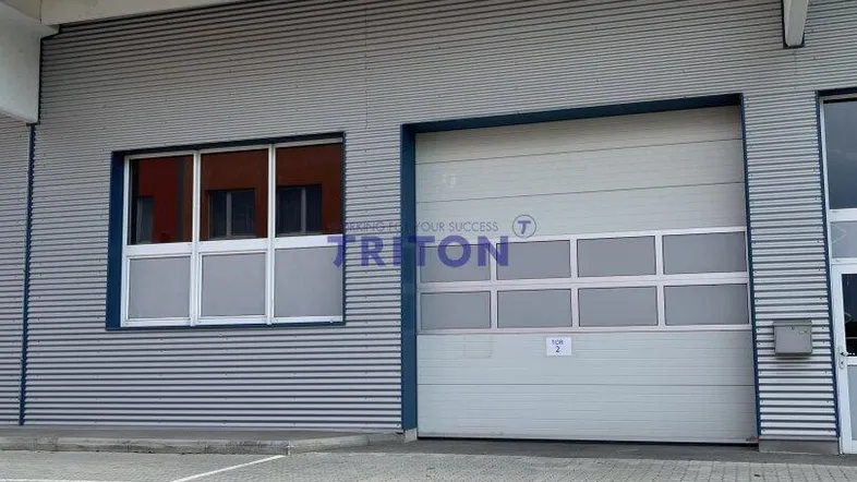 Moderne Gewerbefassade mit großem Garagentor und einem Fensterbereich, umgeben von einer gepflasterten Fläche.