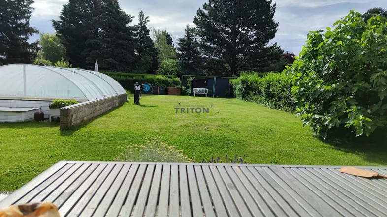 Weitläufiger Garten mit Rasenfläche und überdachtem Pool, gesehen von einem Holztisch.