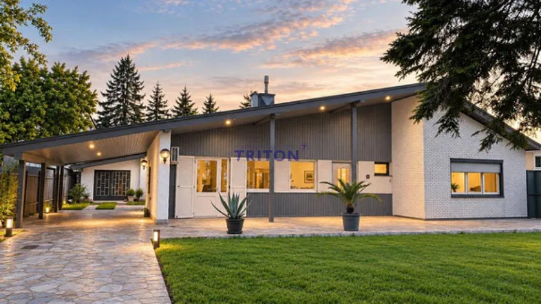 Modernes Haus mit markantem Dach, gepflegtem Rasen und beleuchtetem Eingangsbereich bei Sonnenuntergang.