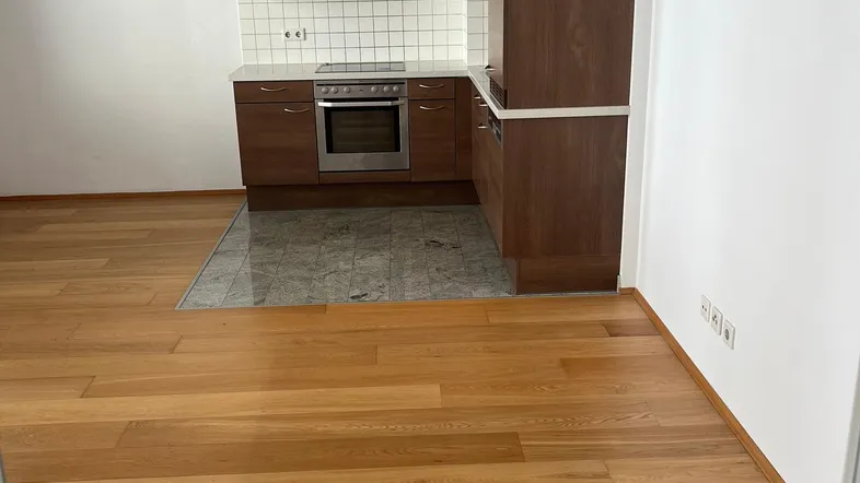 Offener Wohnbereich mit Holzboden und integrierter Küche mit braunen Schränken und weißen Fliesen.