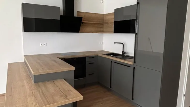 Moderne Küche mit grauen Hochglanzfronten, Holzarbeitsplatte und integriertem Essbereich.