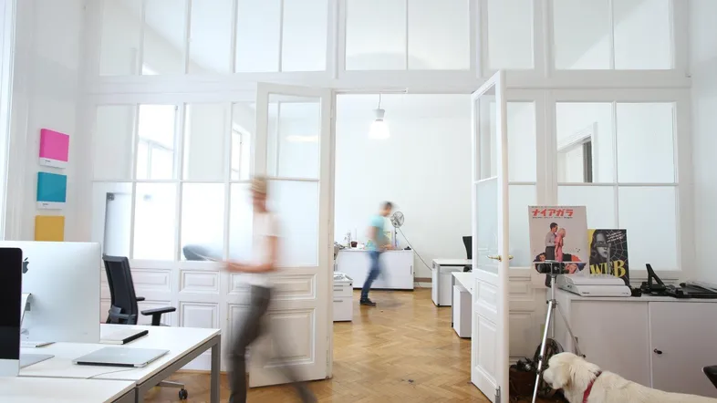 Helles, modernes Büro mit Glasabtrennungen, Holzboden und viel Tageslicht, ideal für kreative Arbeit.