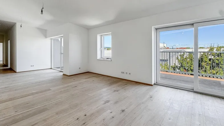 Helles, leeres Zimmer mit Holzboden und Zugang zu einem Balkon, ideal für Wohn- oder Essbereich.