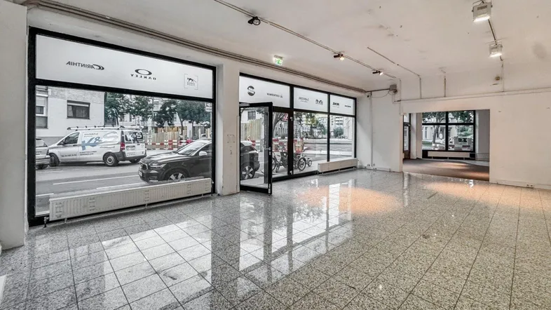 Geräumiger, leerstehender Ladenbereich mit großen Schaufenstern und Fliesenboden, ideal für gewerbliche Nutzung.