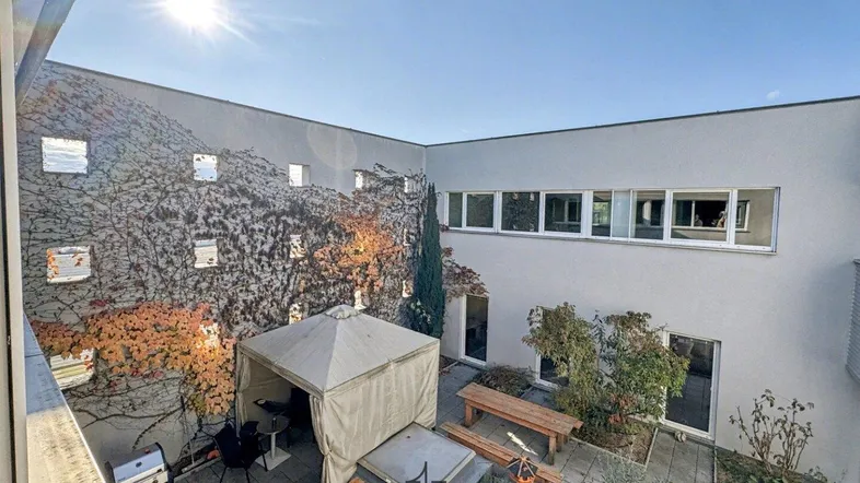 Sonnenverwöhnter Innenhof mit Sitzgelegenheiten, Grillbereich und begrünten Wänden, ideal zum Entspannen im Freien.
