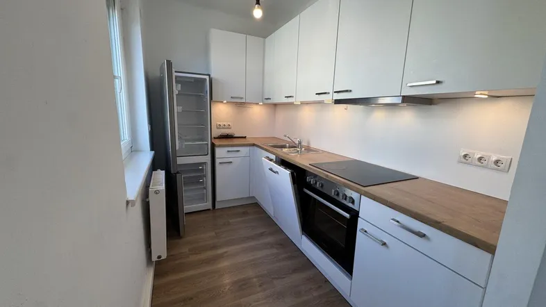 Moderne Einbauküche mit weißen Schränken, Holzarbeitsplatte, Kühlschrank und integrierten Kochgeräten.