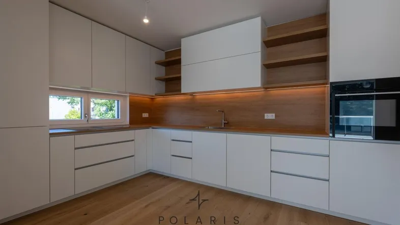 Moderne Küche mit weißen Schränken, Holzrückwand und integrierten Geräten, beleuchtet von Unterbauleuchten.