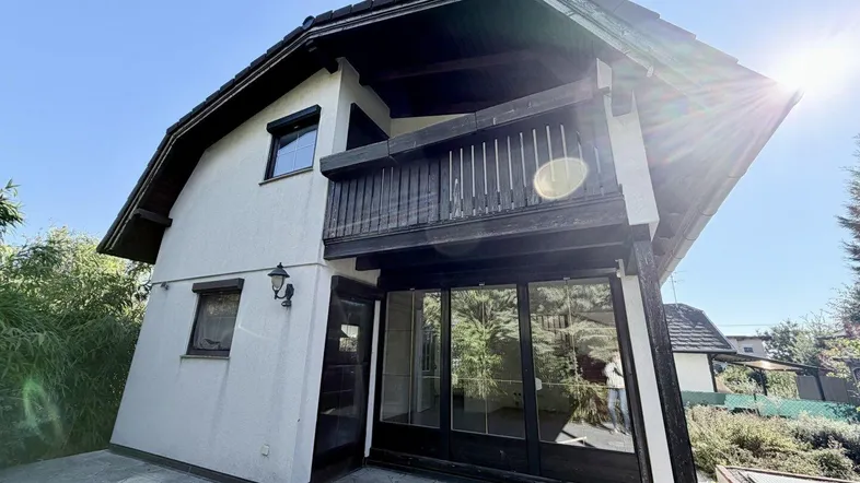 Hausfassade mit Balkon und gepflastertem Bereich unter strahlendem Sonnenschein.