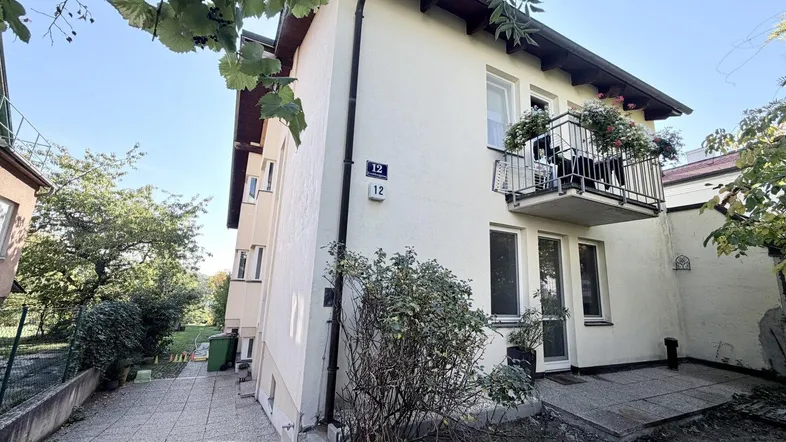 Fassade eines Mehrfamilienhauses mit kleinem Balkon und gepflastertem Zugangsbereich im Freien.