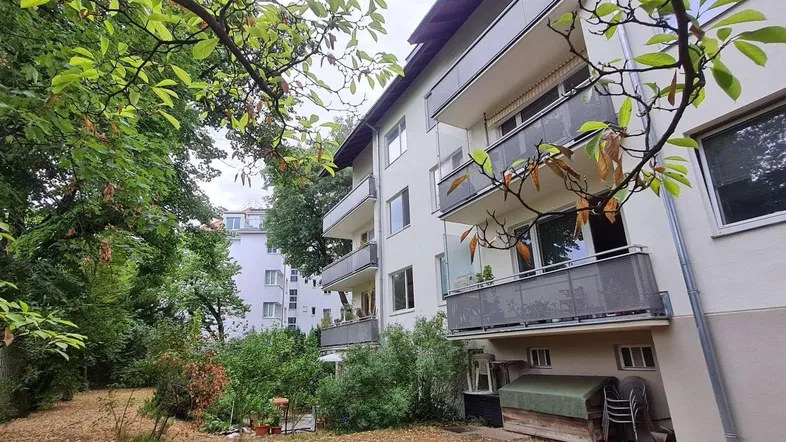 Mehrfamilienhaus mit Balkonen, umgeben von üppigem Grün und Bäumen.