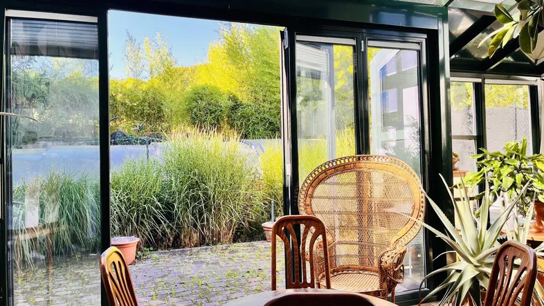 Heller Wintergarten mit Rattanmöbeln und Blick auf den grünen Garten.