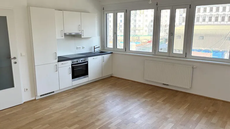 Offener Wohn- und Küchenbereich mit Parkettboden und einer Reihe von Fenstern mit Stadtblick.