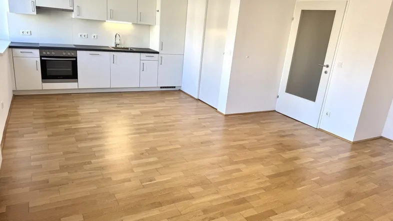 Helle Wohnküche mit modernen weißen Schränken, dunkler Arbeitsplatte und Parkettboden.