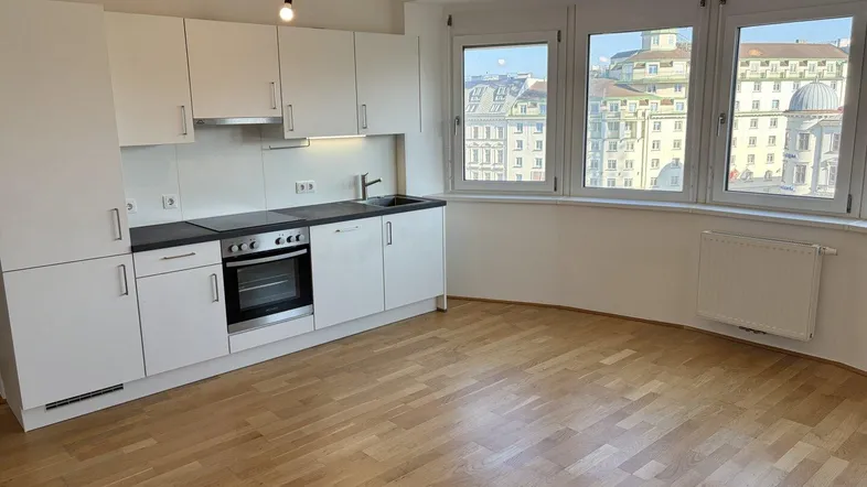 Geräumiger Wohnbereich mit integrierter Küche, Parkettboden und weitem Blick über die Stadt.