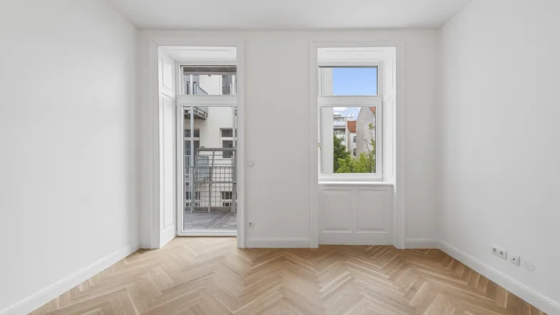 Lichtdurchfluteter Raum mit Fischgrätparkett, Balkontür und großem Fenster.
