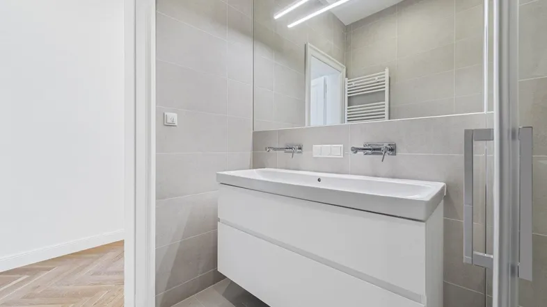 Modernes Badezimmer mit schwebendem Waschtisch, großem Spiegel und Duschbereich, angrenzend an einen Raum mit Fischgrätparkett.