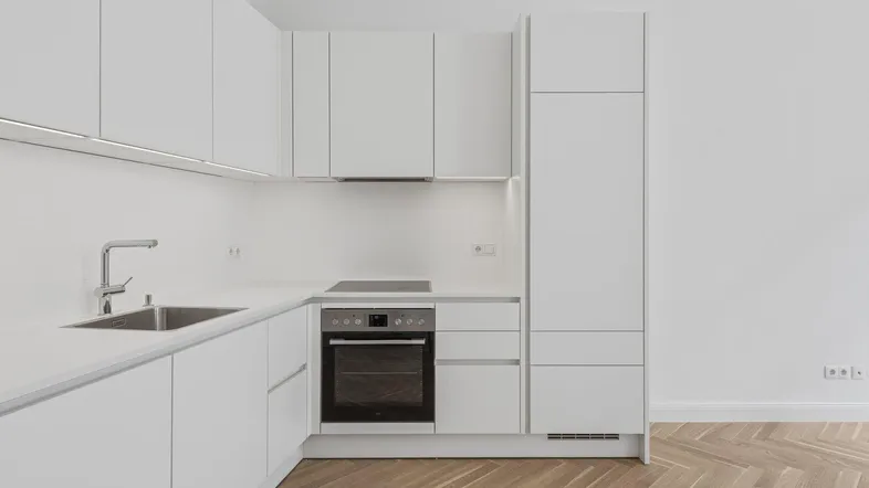 Moderne, helle Küche mit weißen Schränken, integrierten Geräten und Fischgrätparkettboden.