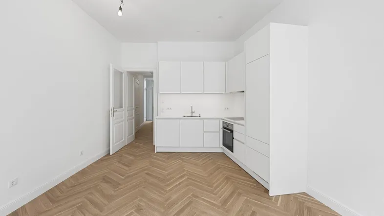 Helle, moderne Küche mit weißen Schränken und Fischgrätparkett in einem offenen Wohnbereich.